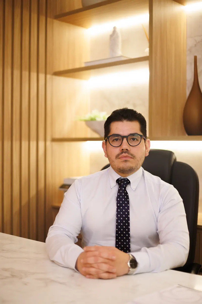 Dr. John Terrazas à mesa do consultório, com as mãos entrelaçadas